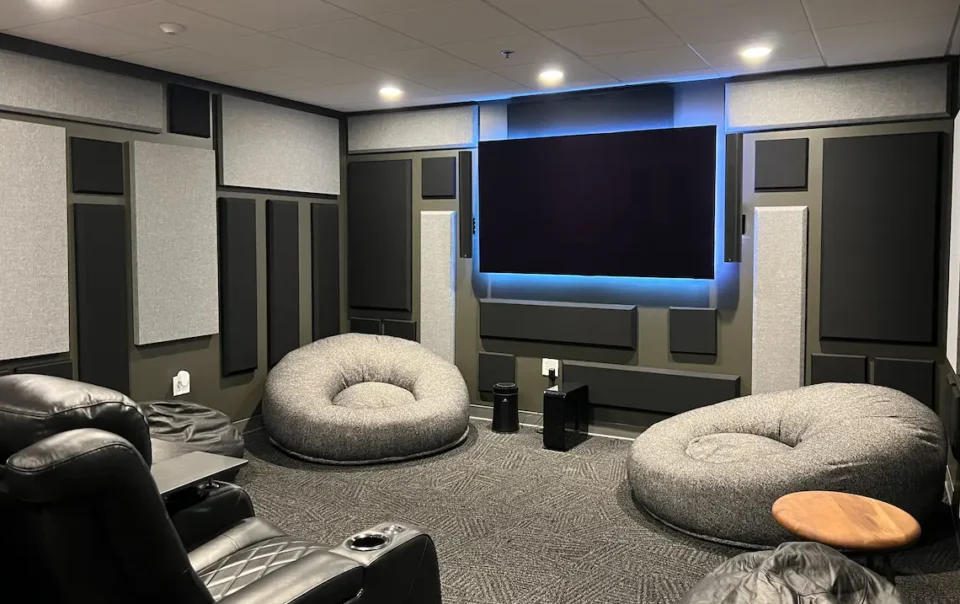 Premium media room with acoustic panels, large wall-mounted display, lounge seating, and integrated AV equipment installed by Macrotek.