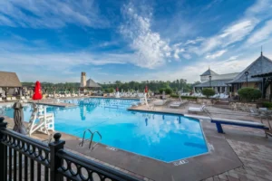 Expansive outdoor pool complex at a private club with diving board, loungers, and landscaped deck under a blue sky