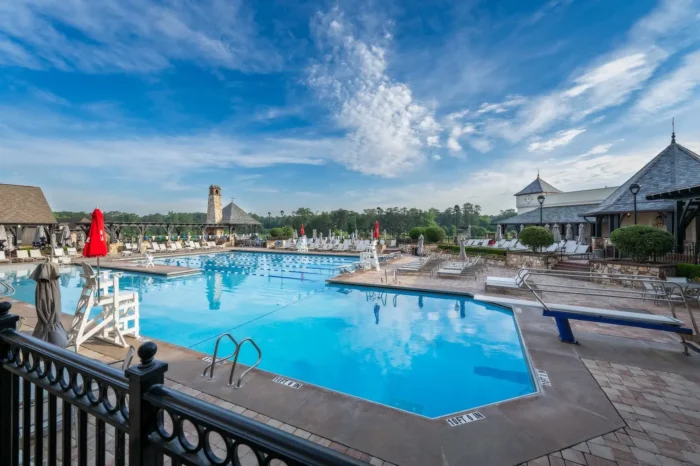 Expansive outdoor pool complex at a private club with diving board, loungers, and landscaped deck under a blue sky