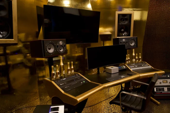Gold-walled recording studio mix position with monitors, speakers, and audio racks